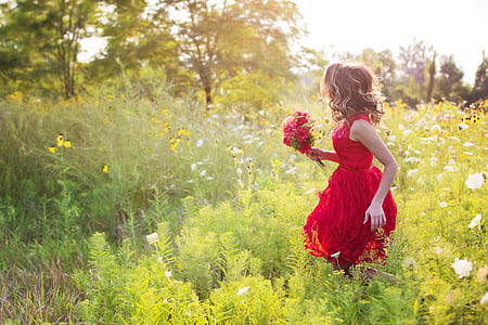 woman wearing dress while carrying bouquet of flower on a flower field