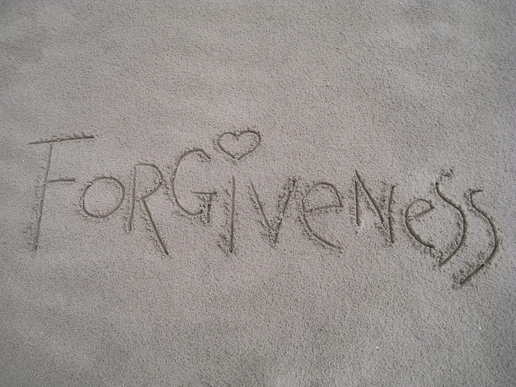 closeup photo of Forgiveness drawn in sand