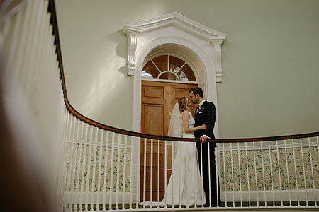 woman in white wedding dress and man black suit kissing together