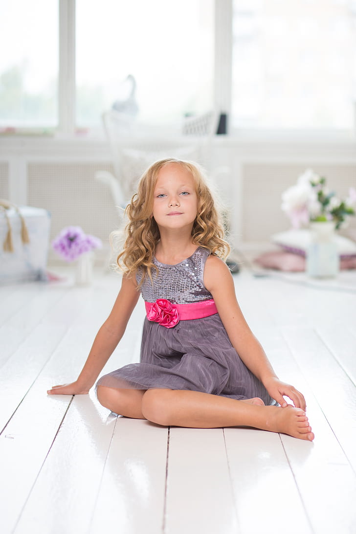 shallow focus photography of a girl in gray sleeveless dress sitting on white tile flooring during daytime