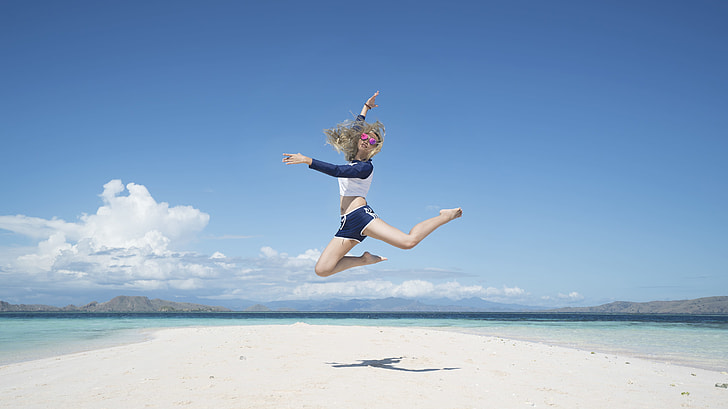 woman jumping near seashore during daytime