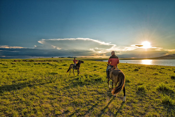 two men rides horse during golden hour