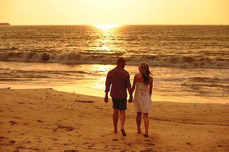 couple holding each other while walking beside beach