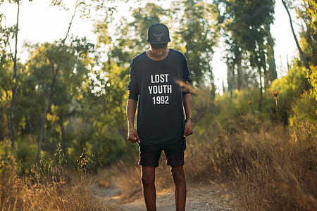 man in black lost youth 1992-printed crew-neck sweater standing between brown grass during daytim