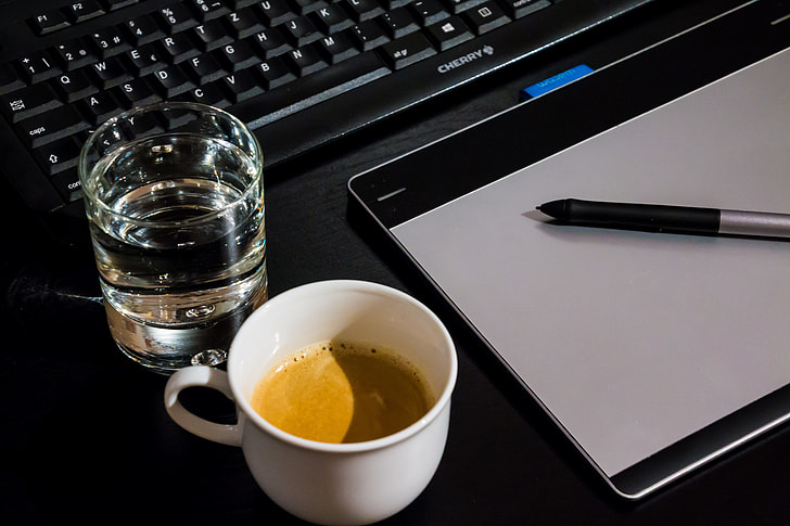 flat lay photograph of clear drinking glass, white ceramic cup, and Wacom Intuos graphics tablet