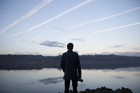 man standing watch calm body of water during daytime