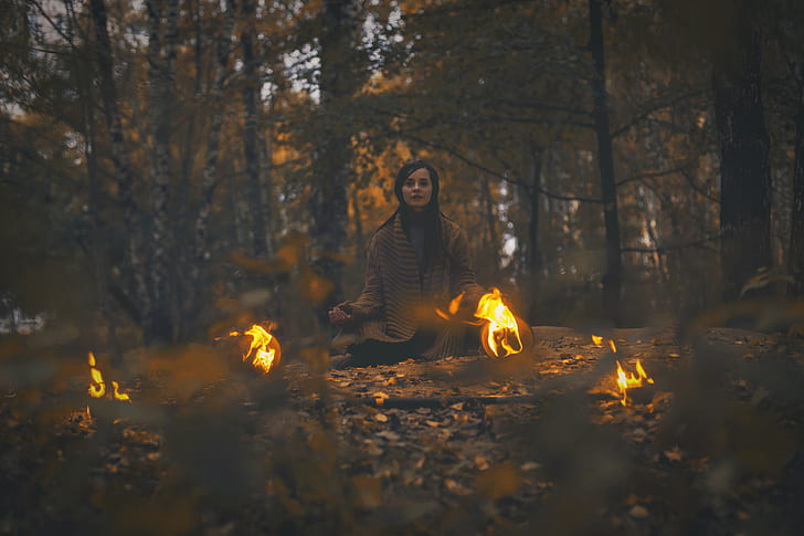 woman wearing brown cardigan sitting in forest surrounded with fireballs