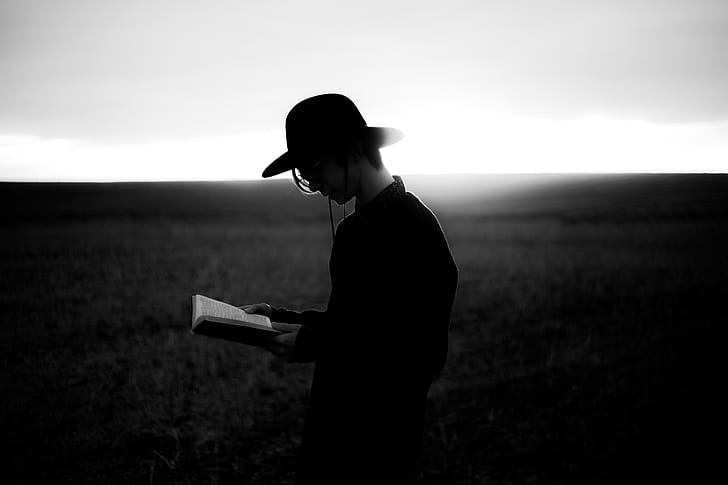 grayscale photography of a person in black dress shirt wearing black hat reading a book