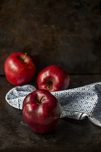 three red apples beside blue and white textile