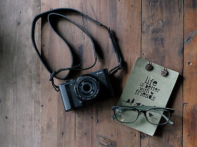 black SLR camera near black reading glasses on brown wooden surface