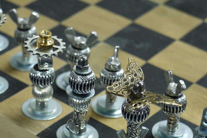 silver-colored gear chess pieces on beige and black board