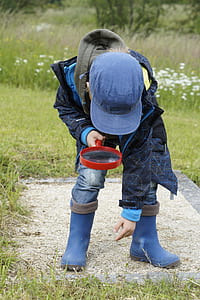 child wearing blue jacket, hat, and boots holding magnifying glass