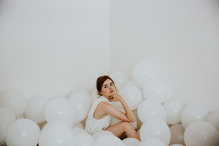 woman wearing sleeveless top sitting on the floor surrounded with white balloons