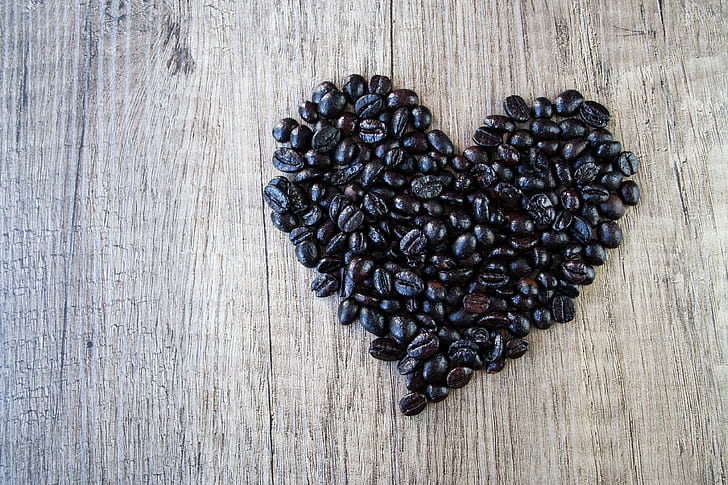 heart-shaped black coffee beans on brown wooden surface