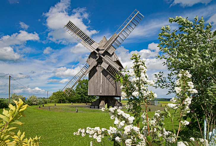 brown wooden windmill in the middle of green grass field under cloudy blue sky during daytime