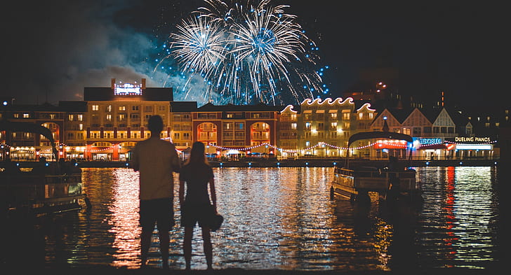 man and woman standing near body of water watching fireworks