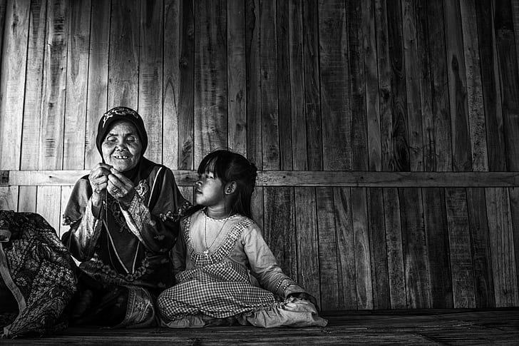 grayscale photo of a woman and child sitting in a corner of a wooden house