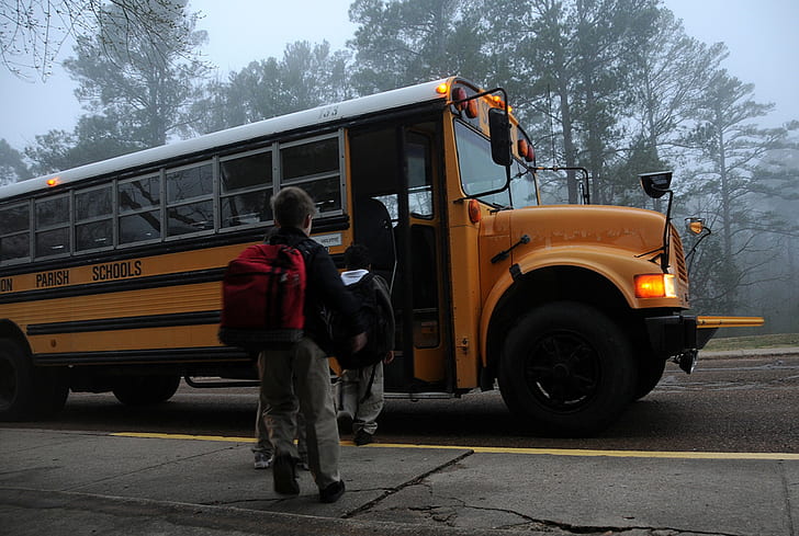 boy carrying black backpack going through yellow school bus