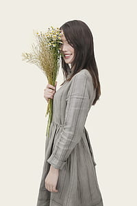 smiling woman wearing gray long-sleeved dress holding a bouquet of flowers