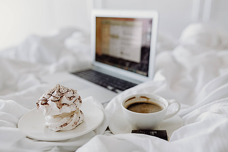 Woman working on a laptop while enjoying a breakfast coffee and chocolate in bed