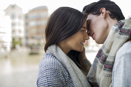 man in purple and brown scarf going to kiss woman beside river