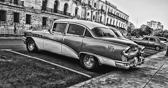 Greyscale Photo of Vintage Car Parked Beside Building