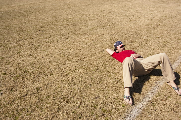 man wearing red t-shirt and brown pants lying on brown grass field