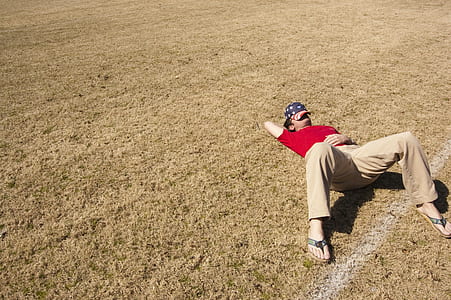 man wearing red t-shirt and brown pants lying on brown grass field