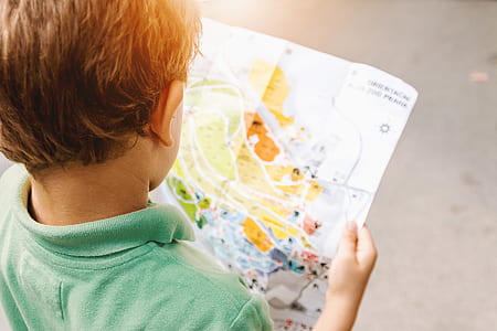 boy in green polo shirt reading map during daytime