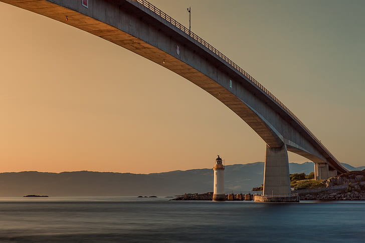 lighthouse under gray bridge during golden hour