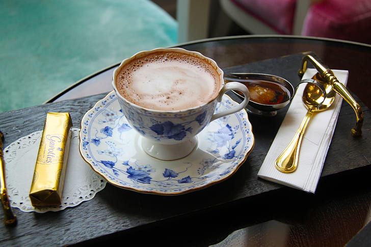 white and blue floral ceramic teacup filled of coffee near chocolate bar and gold-colored spoon
