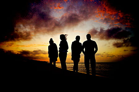 silhouette of four people standing near seashore towards sunset view