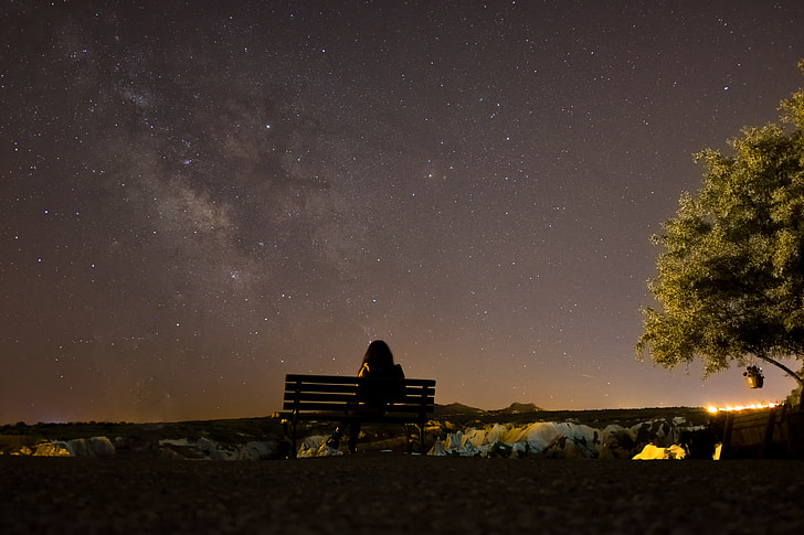 silhouette of a person sitting in the bench watching night sky