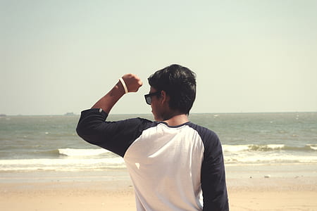 Man in White and Black Raglan Shirt Standing in the Seashore at Daytime