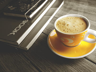 white and yellow ceramic cup filled of coffee beside book