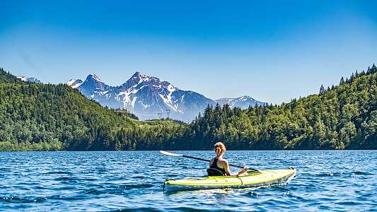 woman kayaking on body of water beside forest and mountains