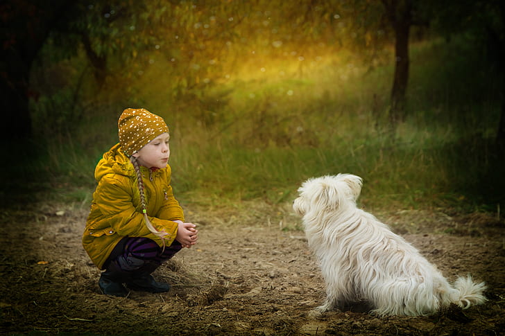 girl in yellow jacket siting front of medium-coated white dog at daytime