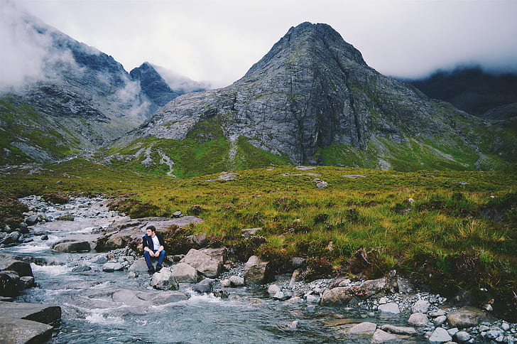 person sitting on gray rock on river