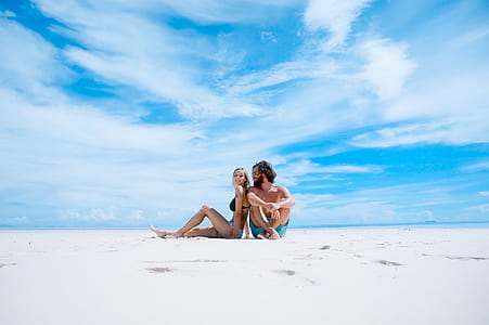 man and woman sitting on white sand during daytime