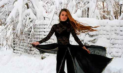 woman in black long-sleeved dress walking on snowfield
