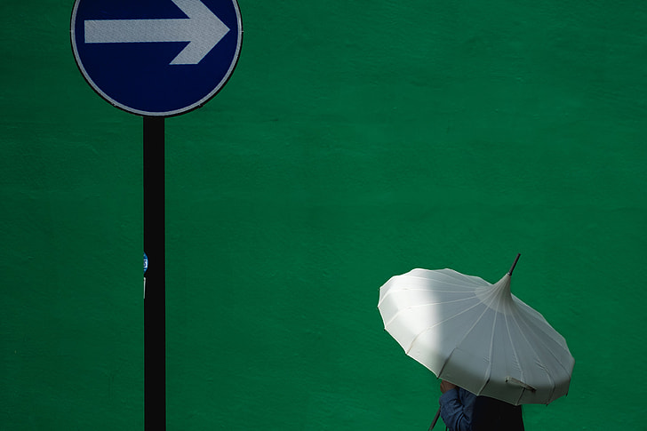 man holding white umbrella nearly on road sign