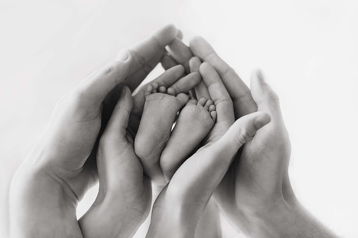 grayscale photo human hands and baby feet