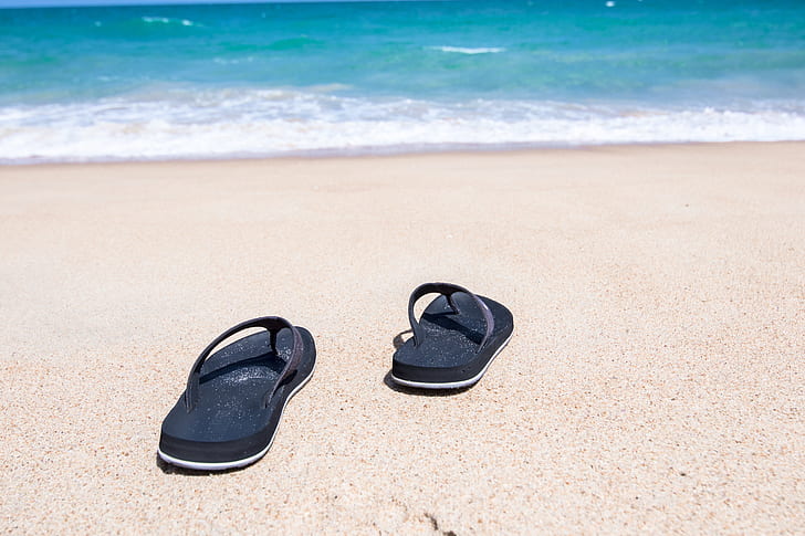 pair of black flip-flops on brown sand along seashore
