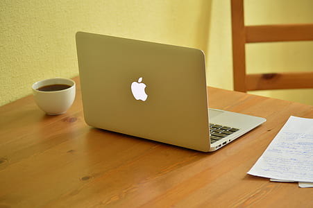MacBook Air beside cup of coffee on brown wooden table