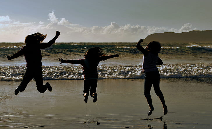 three children's jump shot on front of beach