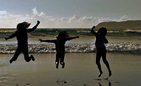 three children's jump shot on front of beach