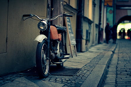 closeup photography of red and black standard motorcycle leaning on gray concrete wall