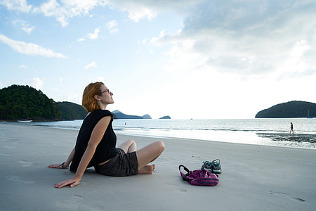 woman wearing black shirt and shorts sitting on seashore watching sea