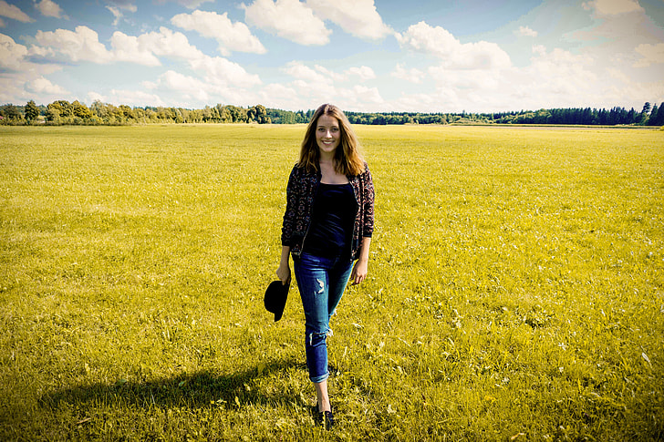woman wearing black shirt and gray cardigan walking on the green grass field