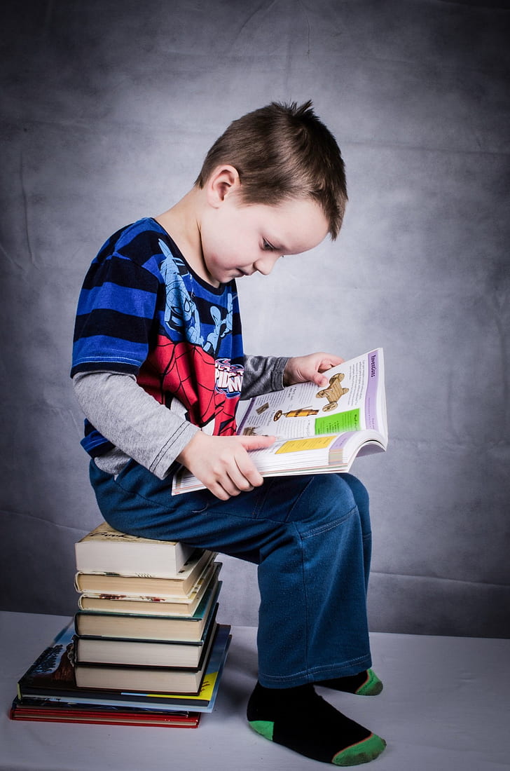 boy reading book sitting on stack of books
